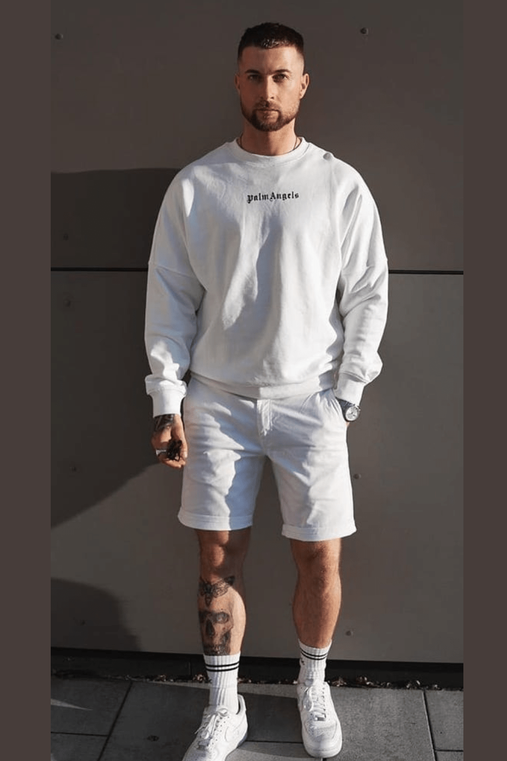 male posing for all white mens outfit with white palm angels brand sweatshirt and white shorts. all white summer outfit