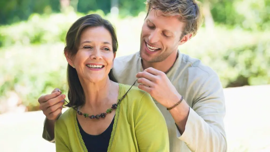 picture of a young man wrapping a necklace around his older girlfriend. 